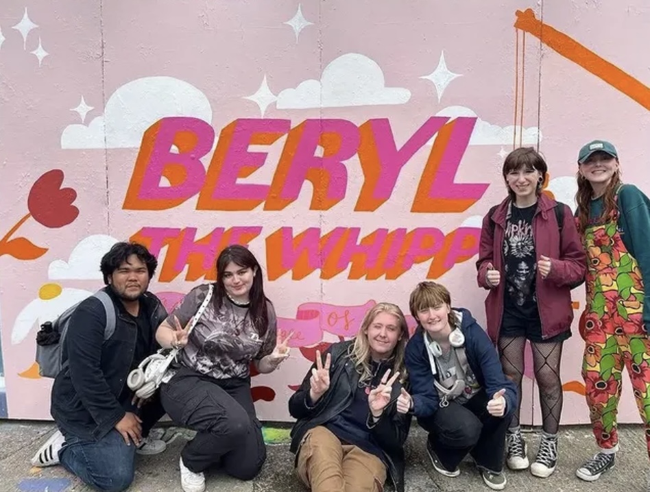 Artists standing in front of a pink mural with bold Berry Whip lettering